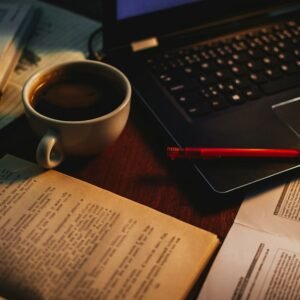 كتب مفتوحة وقلم إلى جانب حاسوب محمول، في مشهد يجمع القراءة والتحرير بالتقنية.